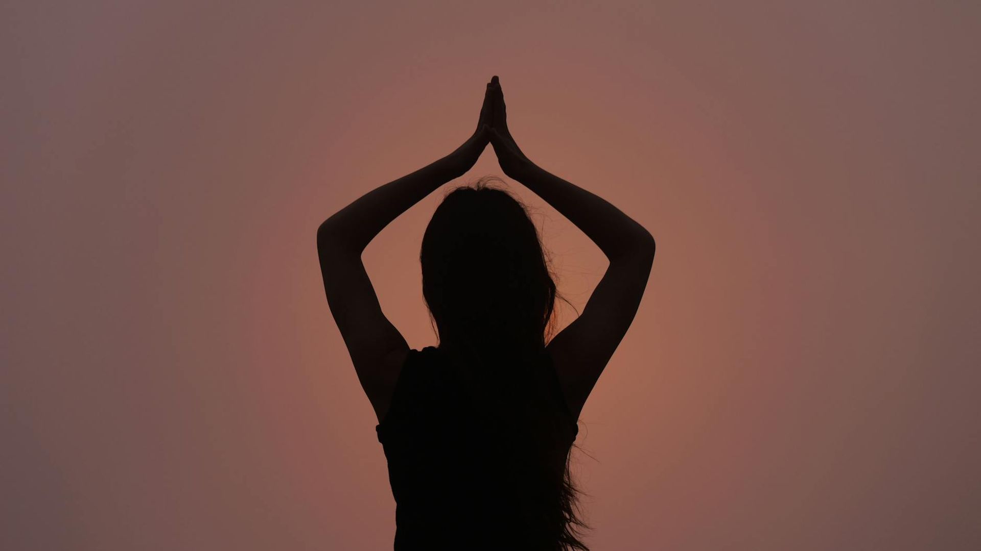 Silhouette of a person in a calm yoga pose against a dark, serene background.